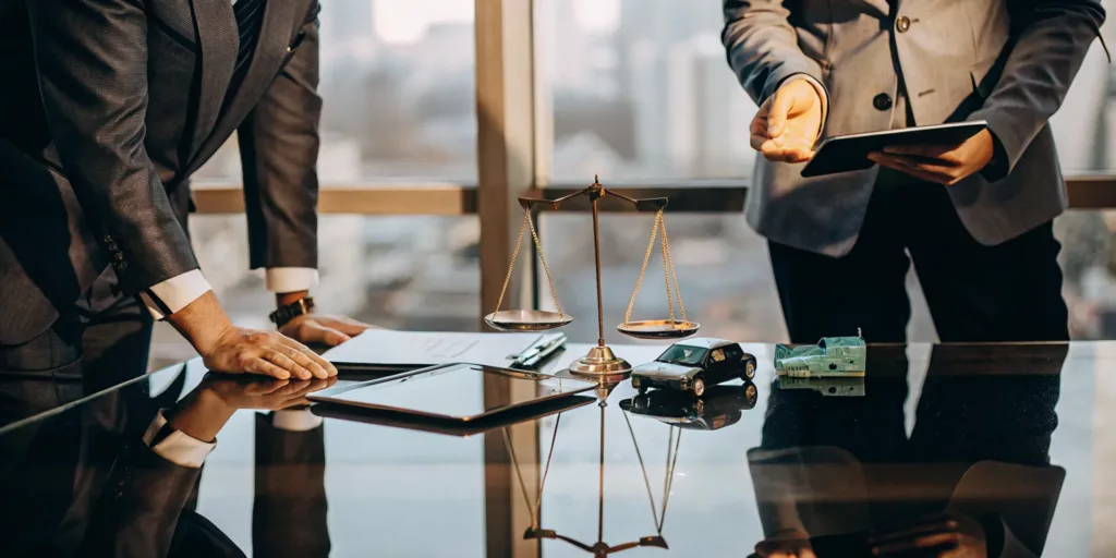 Lawyers calculating a car accident settlement with a toy car, cash, and scales of justice.