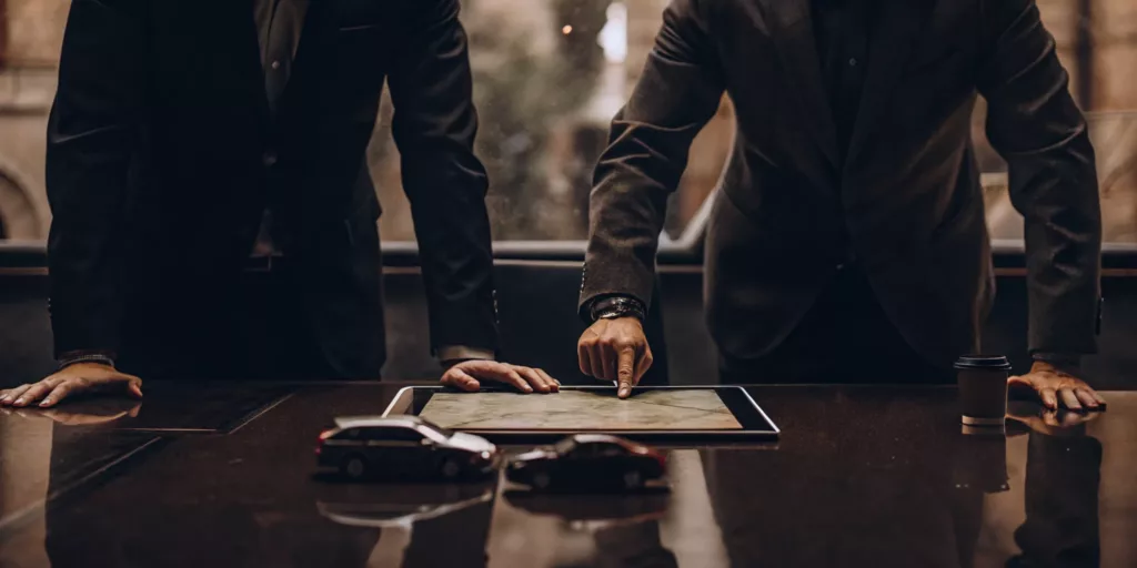 Rideshare accident lawyer evaluates a complex case with a colleague, using a tablet and car models.